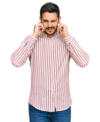 Young hispanic man wearing business shirt covering ears with fingers with annoyed expression for the noise of loud music. deaf concept.