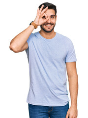 Young hispanic man wearing casual clothes doing ok gesture with hand smiling, eye looking through fingers with happy face.