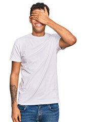 Fototapeta premium Young handsome african american man wearing casual white tshirt smiling and laughing with hand on face covering eyes for surprise. blind concept.