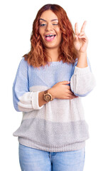 Obraz premium Young latin woman wearing casual clothes smiling with happy face winking at the camera doing victory sign with fingers. number two.