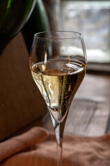Glass of sparkling white wine champagne or cava with bubbles and classic wooden champagne pupitre rack with empty bottles on background