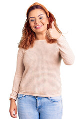 Fototapeta premium Young latin woman wearing casual clothes and diadem doing happy thumbs up gesture with hand. approving expression looking at the camera showing success.