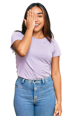 Young latin woman wearing casual clothes covering one eye with hand, confident smile on face and surprise emotion.