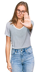 Beautiful young blonde woman wearing casual clothes and glasses doing stop sing with palm of the hand. warning expression with negative and serious gesture on the face.