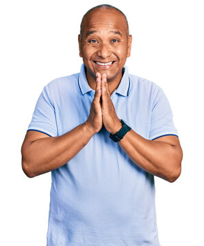 Hispanic middle age man wearing casual t shirt praying with hands together asking for forgiveness smiling confident.
