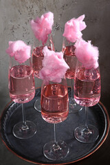 Pink champagne in a tall glass. A few glasses. Champagne is decorated with cotton candy. Drink for the party.