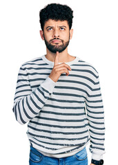 Young arab man with beard wearing casual striped sweater thinking concentrated about doubt with...