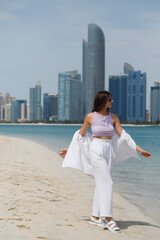 a girl walks on the beach against the background of buildings in Abu Dhabi