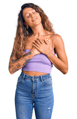 Young hispanic woman with tattoo wearing casual clothes smiling with hands on chest with closed eyes and grateful gesture on face. health concept.