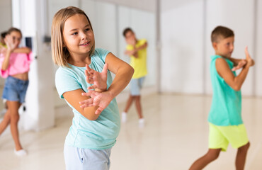 Young girl and her friends performing modern dance in studio during rehearsal.