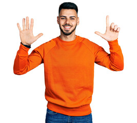 Young hispanic man with beard wearing casual orange sweater showing and pointing up with fingers number seven while smiling confident and happy.