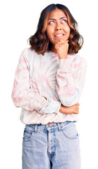 Young beautiful mixed race woman wearing casual tie dye sweatshirt with hand on chin thinking about question, pensive expression. smiling with thoughtful face. doubt concept.