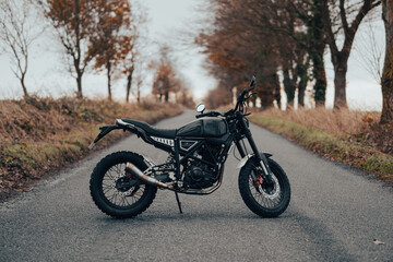 Scrambler motorcycle off-road machine, motorbike parked on a forest road with autumn trees and leaves