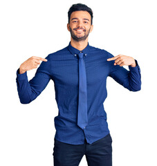 Young handsome hispanic man wearing business clothes looking confident with smile on face, pointing...