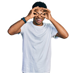 Young african american man wearing casual white t shirt doing ok gesture like binoculars sticking tongue out, eyes looking through fingers. crazy expression.