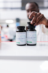 Vitamins bottles on drugstore shelf closeup, selective focus, african american pharmacist taking supplements. Pharmacy medic putting pills close view, medicaments selling, pharmaceutical service