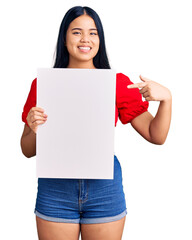 Young beautiful asian girl holding blank empty banner smiling happy pointing with hand and finger