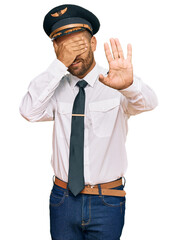 Handsome man with beard wearing airplane pilot uniform covering eyes with hands and doing stop gesture with sad and fear expression. embarrassed and negative concept.