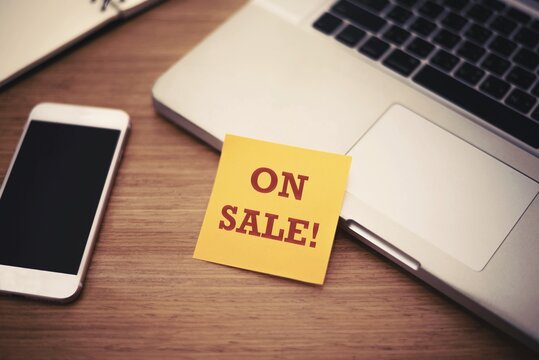 "On sale" text on post it paper near laptop and smart phone on wood table, Online shopping and Technology marketing concept. Split and cross processing tone pinterest and instragram like process.