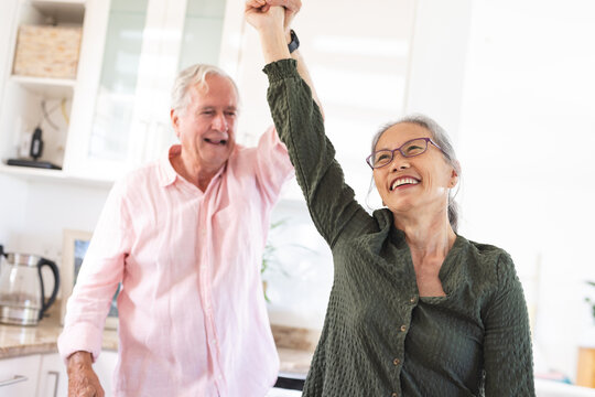 Happy senior diverse couple dancing together in kitchen