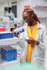 Plakat African american woman checking multi vitamins in drugstore shelf, looking at tablet packages. Client choosing nutritional supplements, customer standing in pharmacy store aisle