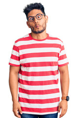 Obraz premium Handsome latin american young man wearing casual clothes and glasses making fish face with lips, crazy and comical gesture. funny expression.