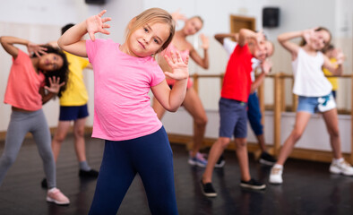 Fototapeta na wymiar Portrait of cheerful preteen girl practicing dance movements with group of children in choreography class