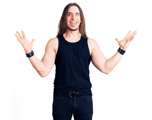 Young adult man with long hair wearing rocker style with black clothes and contact lenses celebrating victory with happy smile and winner expression with raised hands