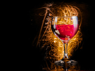 Glass or red wine, dark background with golden fire light painting effect. Alcohol product for a special occasion.