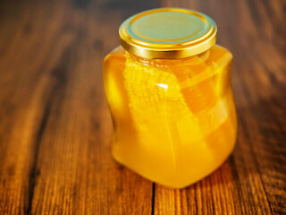 Glass jar of honey with honeycomb inside on a wooden surface,. Selective focus. Top high quality product. Rich golden yellow color.