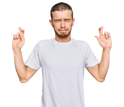 Hispanic young man wearing casual white t shirt gesturing finger crossed smiling with hope and eyes closed. luck and superstitious concept.