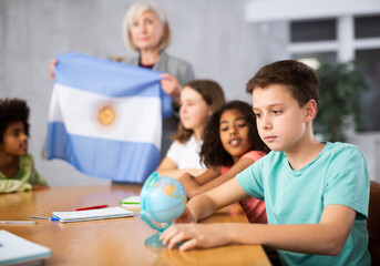 Ten-year-old schoolboy is studying the history of Argentina in lesson and attentively is looking for it on the globe