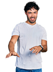 Hispanic young man with beard wearing casual white t shirt disgusted expression, displeased and fearful doing disgust face because aversion reaction.