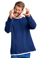 Handsome blond man with beard wearing casual sweater shouting frustrated with rage, hands trying to strangle, yelling mad