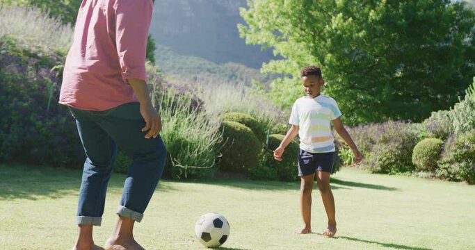 Happy african american father and son playing soccer in garden, in slow motion