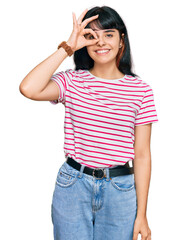 Young hispanic girl wearing casual clothes doing ok gesture with hand smiling, eye looking through fingers with happy face.