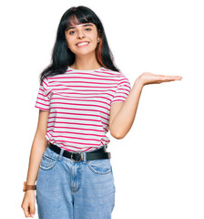 Young hispanic girl wearing casual clothes smiling cheerful presenting and pointing with palm of hand looking at the camera.