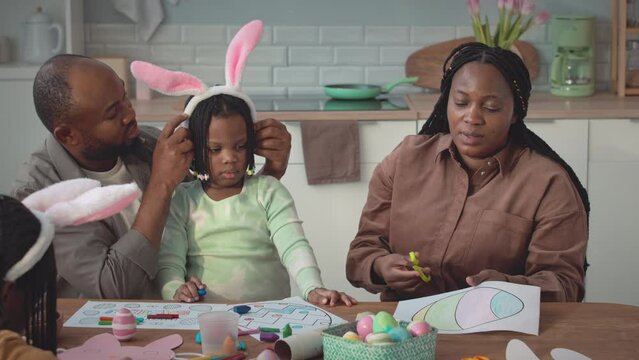 Modern African American family of four celebrating Easter together at cozy home. Girls wearing cute bunny ears headbands
