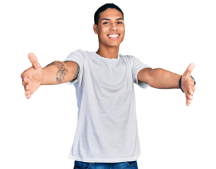 Young hispanic man wearing casual white t shirt looking at the camera smiling with open arms for hug. cheerful expression embracing happiness.