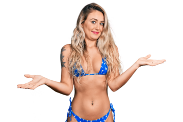 Young blonde woman wearing bikini clueless and confused expression with arms and hands raised. doubt concept.