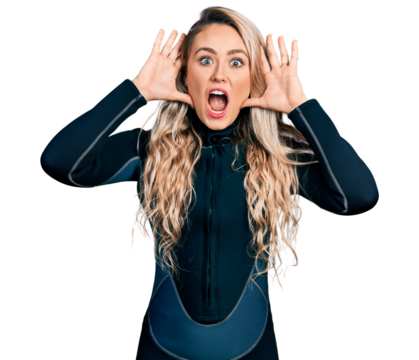 Young blonde woman wearing diver neoprene uniform smiling cheerful playing peek a boo with hands showing face. surprised and exited