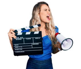 Young blonde woman holding video film clapboard and megaphone angry and mad screaming frustrated and furious, shouting with anger. rage and aggressive concept.