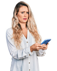 Young blonde woman using smartphone clueless and confused expression. doubt concept.