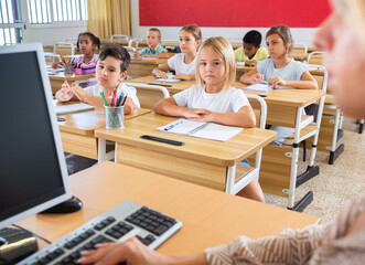 Fototapeta premium Portrait of diligent towheaded preteen girl looking at camera during lesson in primary school