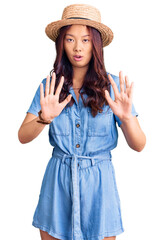 Young beautiful chinese girl wearing summer hat moving away hands palms showing refusal and denial with afraid and disgusting expression. stop and forbidden.