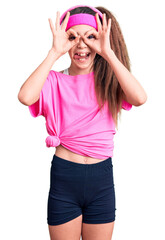 Obraz na płótnie Canvas Cute hispanic child girl wearing gym clothes and using headphones doing ok gesture like binoculars sticking tongue out, eyes looking through fingers. crazy expression.