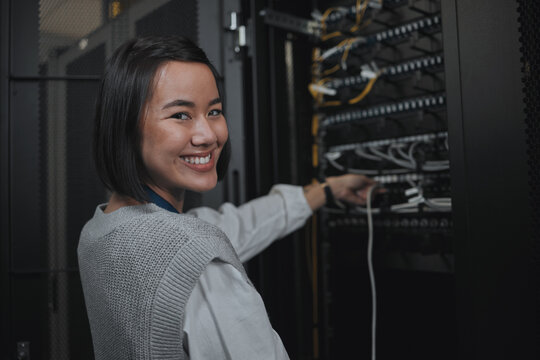Asian woman, portrait smile and technician by server for cabling, networking or system maintenance at office. Happy female engineer smiling in cable service, power or data management or admin control