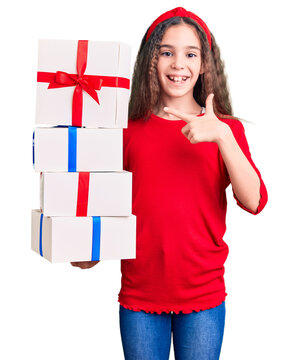 Cute hispanic child girl holding gift smiling happy pointing with hand and finger
