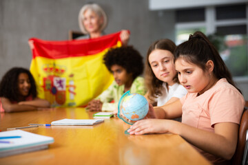 in geography lesson, pupils carefully listen to woman teacher who talks about Spain