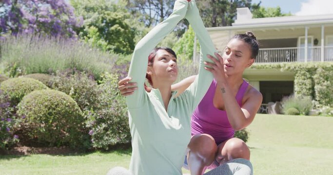 Happy biracial sisters doing yoga and meditating in garden, in slow motion